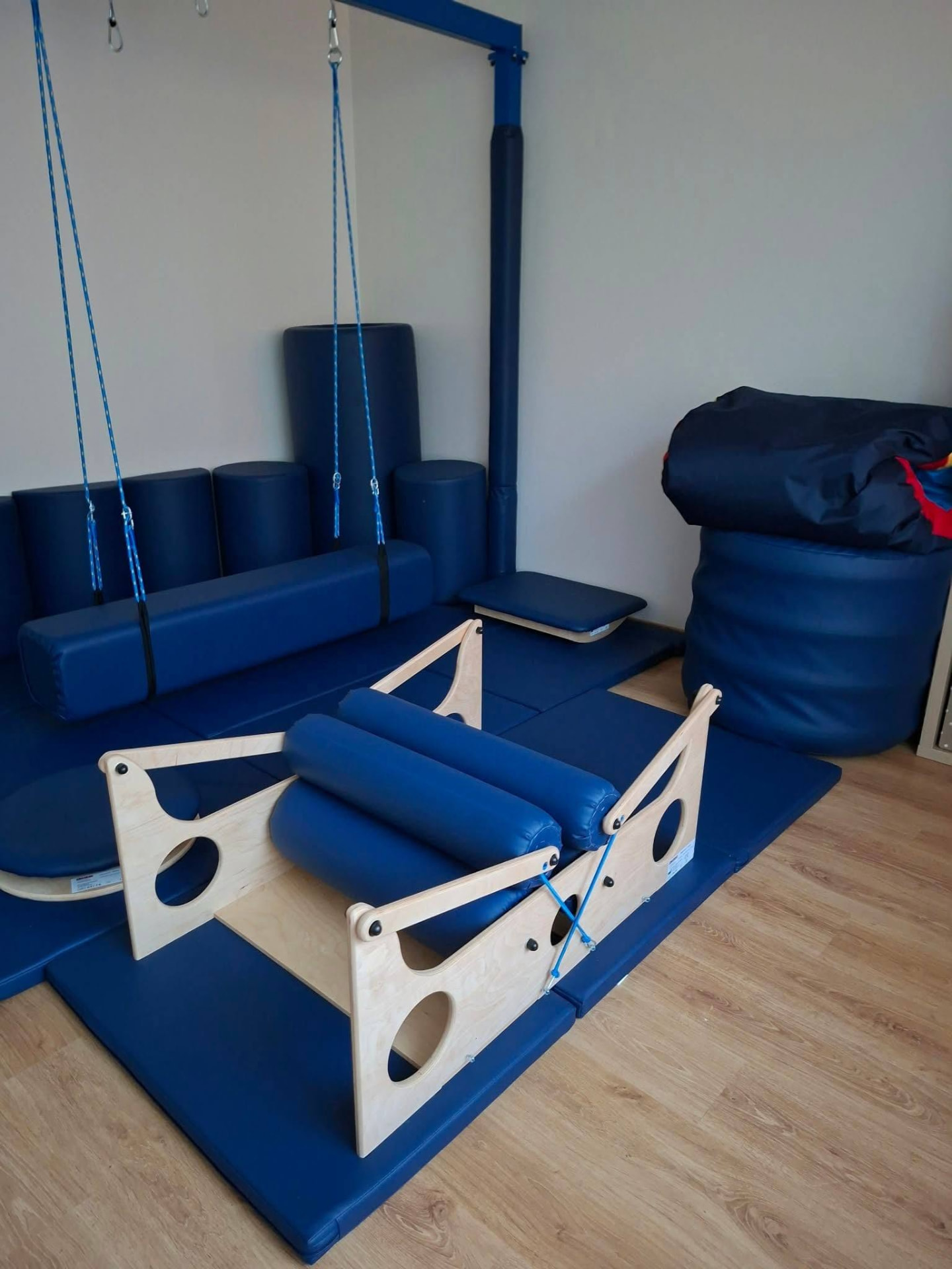 A therapy and play room with soft blue mats, rollers and a swing