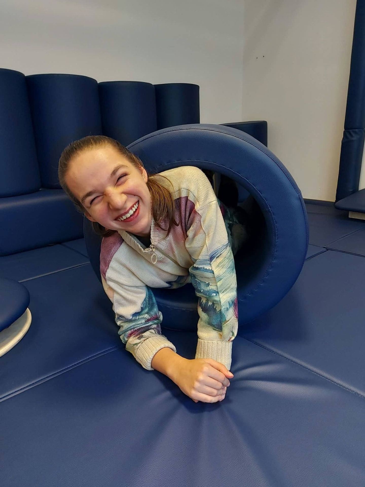A young person laughing while crawling through a soft play tunnel